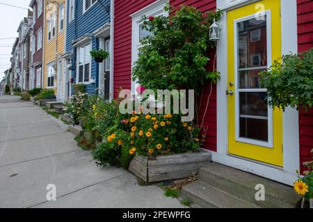 Vue sur la rue et le trottoir de plusieurs bâtiments en bois colorés de différentes couleurs. Les petites structures ont des fenêtres à double accrocher et des portes blanches. Banque D'Images