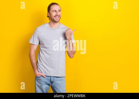 Photo de bonne humeur mec de rêve habillé t-shirt gris regardant pointant pouce emtpy espace isolé couleur jaune arrière-plan Banque D'Images