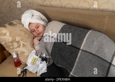 Fille avec des symptômes de rhume se trouve sur un canapé à côté des médicaments. Maux de tête, température élevée. Concept de la médecine, de la pharmacie, des soins de santé et du traitement à domicile Banque D'Images