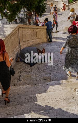 Rome, Italie mendiant gitan avec foulard tenant rosaire sur les marches espagnoles, entouré par la foule passant. Banque D'Images