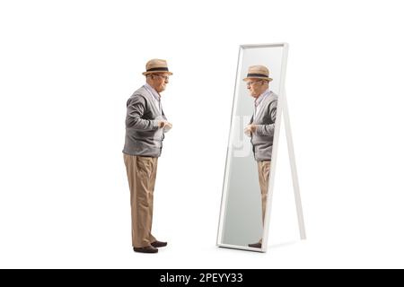 Prise de vue en longueur d'un homme senior qui appuie son chandail devant un miroir isolé sur fond blanc Banque D'Images