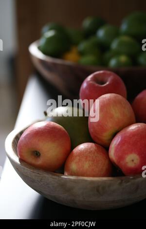 Une table en bois présente un bol de fruits frais variés, y compris des pommes et des limes Banque D'Images