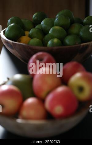 Une table en bois présente un bol de fruits frais variés, y compris des pommes et des limes Banque D'Images