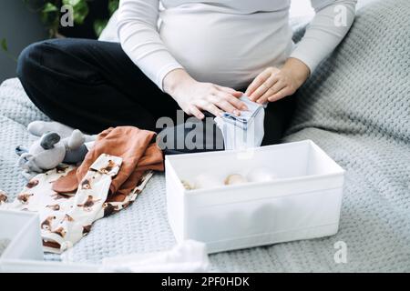 Femme enceinte avec grand ventre tenant body et triant des vêtements pour l'avenir. Comment organiser les vêtements pour nouveau-nés. Préparer les choses pendant la grossesse Banque D'Images