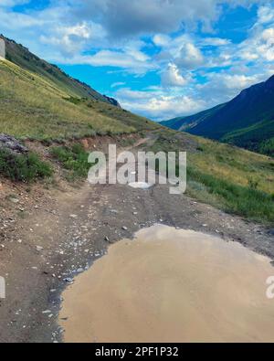 Une route avec une grande flaque sur le bord d'une colline à une falaise va au-dessus de la montagne sous d'épais nuages dans l'Altai en Sibérie Banque D'Images