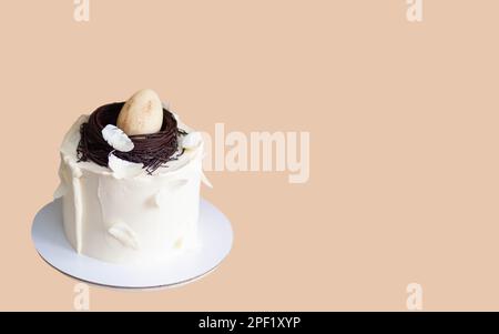Gâteau de pâques élégant décoré avec un nid d'oiseau en chocolat, un œuf et des plumes. Arrière-plan orange avec espace de copie. Orientation horizontale Banque D'Images