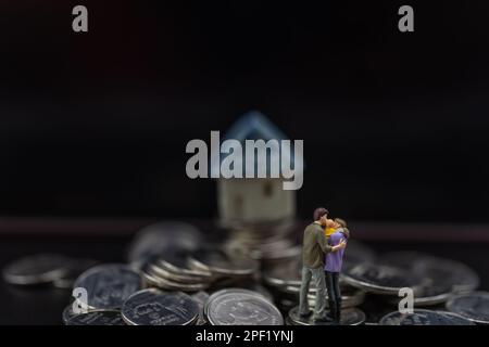 Money, Financial, Business and Family concept, miniature figures homme, femme et enfant se tiennent sur pile de pièces de monnaie avec mini-modèle de jouet de maison sur fond noir Banque D'Images