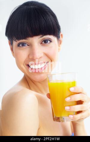 Obtenir sa dose quotidienne de vitamine C. Portrait d'une jeune femme souriante appréciant un verre de jus d'orange. Banque D'Images