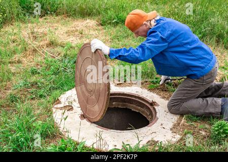 l'homme a ouvert le couvercle de l'orifice d'égout pour pomper les eaux usées. Banque D'Images