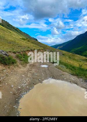 La route des voyageurs avec une grande flaque sur le bord d'une colline près d'une falaise va au-dessus de la montagne sous d'épais nuages dans l'Altai en Sibérie Banque D'Images