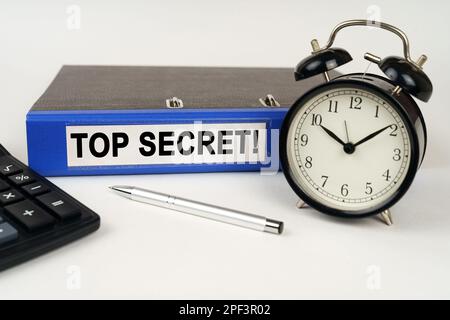 Concept d'entreprise. Sur une surface blanche, un calculateur de réveil et un dossier avec l'inscription - Top Secret Banque D'Images