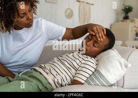 Affectueuse femme afro-américaine inquiète mère prenant soin de l'enfant malade fils à la maison Banque D'Images