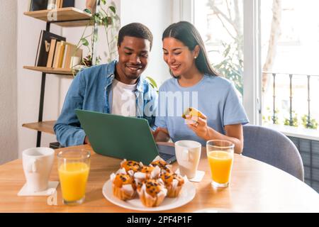 Couple faire l'achat en ligne avec l'ordinateur tout en prenant le petit déjeuner, à côté de la fenêtre, shopping sur Internet Banque D'Images