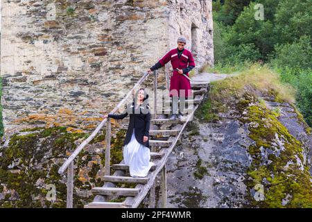 Couple géorgien en robe traditionnelle descendant les escaliers en bois de la Tour de l'Amour, pour usage éditorial seulement, Ushguli, région de Svanetia, Géorgie Banque D'Images