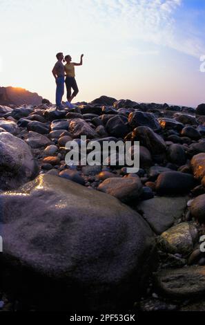 Silhouette d'un couple debout sur une plage rocheuse au lever du soleil Banque D'Images
