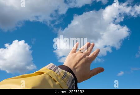 Main adulte se dirigeant vers le ciel. Touchez à la main le ciel bleu avec des nuages. Personne, mise au point sélective, espace de copie pour le texte Banque D'Images