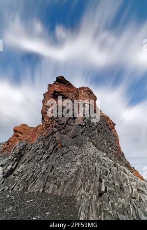 Vue d'en dessous sur une roche en pierre de lave avec des structures de basalte clairement visibles, roche brun rougeâtre dans la partie supérieure, ciel bleu dramatique, le clou Banque D'Images