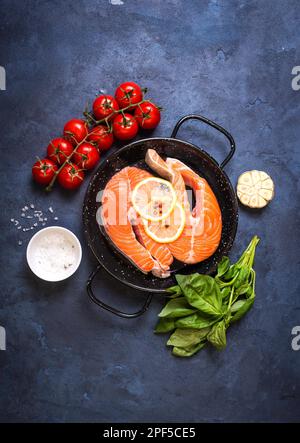 Poisson frais cru avec des légumes prêts à cuire. Steaks de saumon crus avec citron, épices et herbes dans une casserole. Ingrédients pour cuisiner sur un béton rustique Banque D'Images