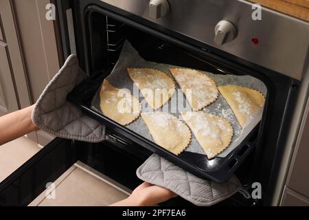 Femme mettant la plaque de cuisson avec des empanadas de viande dans le four, gros plan Banque D'Images