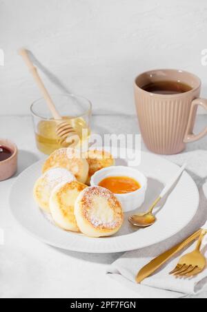 Assiette avec crêpes savoureuses au fromage cottage, confiture, miel et tasse de thé sur fond clair, en gros plan Banque D'Images