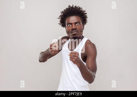 Mécontent impassionnée, homme qui combat avec quelqu'un, regarde la caméra, les poings serrés, a une expression furieuse du visage. Porter un t-shirt blanc. Prise de vue en studio isolée sur fond gris. Banque D'Images