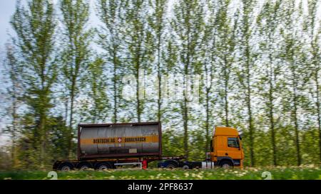 Camion tirant un conteneur-citerne roulant le long d'une route A rurale bordée d'arbres par une journée ensoleillée Banque D'Images