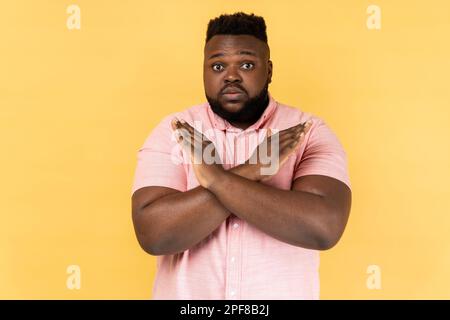 Non, absolument pas. Portrait de l'homme émerveillé portant une chemise rose montrant x signe avec les mains croisées, ce qui signifie arrêt, c'est la fin Studio d'intérieur isolé sur fond jaune. Banque D'Images