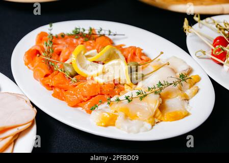 Filets de poisson gras en tranches. Saumon fumé avec tranches de citron et filets de flétan avec grands câpres. Produit utile riche en oméga-3. Banque D'Images
