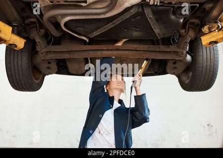 Assurez-vous que votre voiture est en bon état et qu'elle fonctionne en douceur et en toute sécurité. une femme mécanicien travaillant sous une voiture soulevée. Banque D'Images