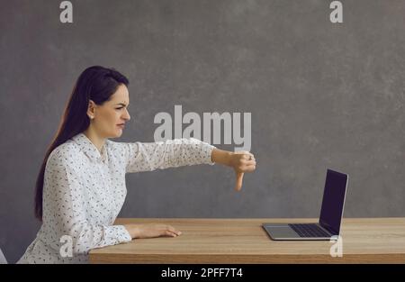 Mécontentement femme utilisant un ordinateur portable et montrant son aversion en donnant des pouces vers le bas à l'écran Banque D'Images