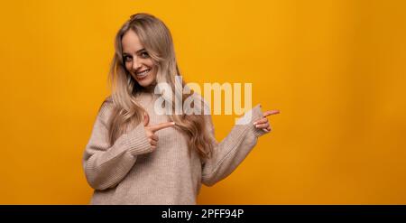 une jeune femme européenne rapporte des informations sur le mur sur fond orange studio Banque D'Images