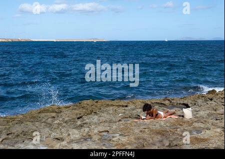 10 juin 2022: Italie, Sardaigne, Sassari, Porto Torres, Femme lit un livre sur les rochers du front de mer de Porto Torres. Banque D'Images