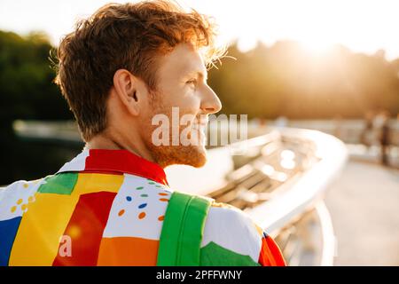 Portrait d'un jeune homme souriant beau regardant de côté, tout en se tenant debout avec son dos à l'appareil photo au soleil Banque D'Images