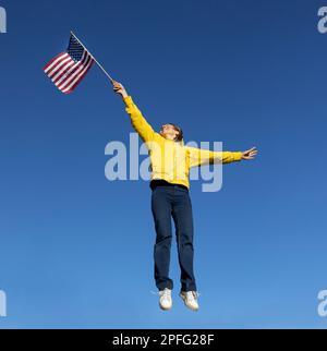 bonne femme active sautant joyeusement contre le ciel bleu sans nuages. Levez le drapeau américain à la main. Célébration de la Journée de l'indépendance des États-Unis. décollage Banque D'Images