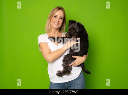 Portrait de jolie gaie et attentive fille tenant dans les mains doggy schnauzer isolé sur fond vert clair de couleur Banque D'Images