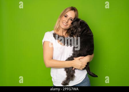 Portrait de jolie gaie et attentive fille tenant dans les mains doggy schnauzer isolé sur fond vert clair de couleur Banque D'Images