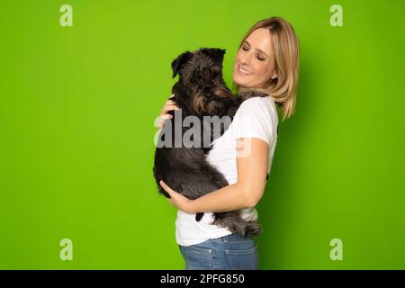 Portrait de jolie gaie et attentive fille tenant dans les mains doggy schnauzer isolé sur fond vert clair de couleur Banque D'Images