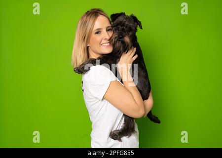 Portrait de jolie gaie et attentive fille tenant dans les mains doggy schnauzer isolé sur fond vert clair de couleur Banque D'Images