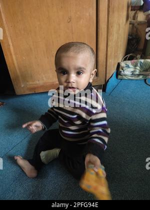 Asiatique mignon bébé assis et jouant un petit jouet sur un tapis doux à la maison. L'enfant tenant le jouet et la question sur la façon du jouer. Banque D'Images