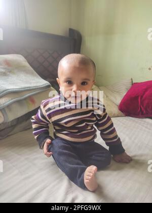 Asiatique mignon bébé assis et jouant un petit jouet sur un tapis doux à la maison. L'enfant tenant le jouet et la question sur la façon du jouer. Banque D'Images