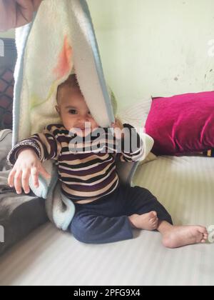 Asiatique mignon bébé assis et jouant un petit jouet sur un tapis doux à la maison. L'enfant tenant le jouet et la question sur la façon du jouer. Banque D'Images