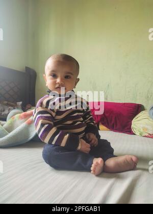 Asiatique mignon bébé assis et jouant un petit jouet sur un tapis doux à la maison. L'enfant tenant le jouet et la question sur la façon du jouer. Banque D'Images