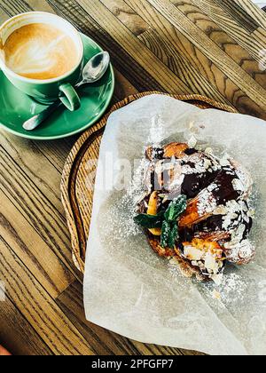 Une bonne tasse de cappuccino avec un croissant sur une table en bois. Petit-déjeuner traditionnel avec café et pâtisseries fraîches Banque D'Images