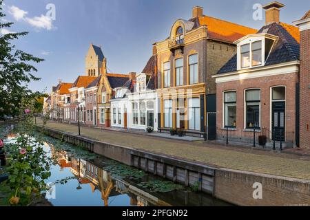 Vieilles maisons traditionnelles colorées le long du canal et en arrière-plan la tour de l'église martini dans la ville pittoresque de Bolsward en Frise Banque D'Images