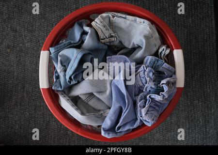 Pantalons en denim, pantalons en denim dépliés propres dans un panier rouge sur un tapis jaune. Photo d'idée de concept de vêtements en denim désordonnée. Vue de dessus d'un panier rouge. Banque D'Images