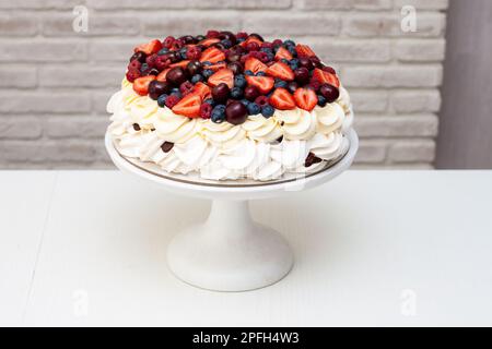 Gâteau à la meringue Pavlova avec crème fouettée et baies fraîches, fraises, bleuets, framboises et cerises sur fond blanc. Banque D'Images