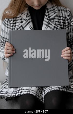 Une jeune fille de 10 ans est assise, tenant un livre photo en cuir gris avec une empreinte de mémoire entre ses mains. Banque D'Images