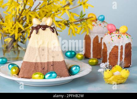 Dessert traditionnel de Pâques caillé composé de trois types de chocolat - blanc, lait et foncé et ainsi que deux gâteaux de Pâques sur fond bleu clair Banque D'Images