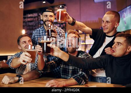 Applaudissent en frappant des verres à bière. Groupe de personnes ensemble à l'intérieur dans le pub ont le plaisir à l'heure du week-end Banque D'Images