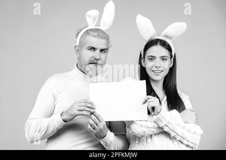 Le couple de Pâques tient un tableau blanc vierge pour votre texte. Portrait du couple de Pâques heureux. Banque D'Images